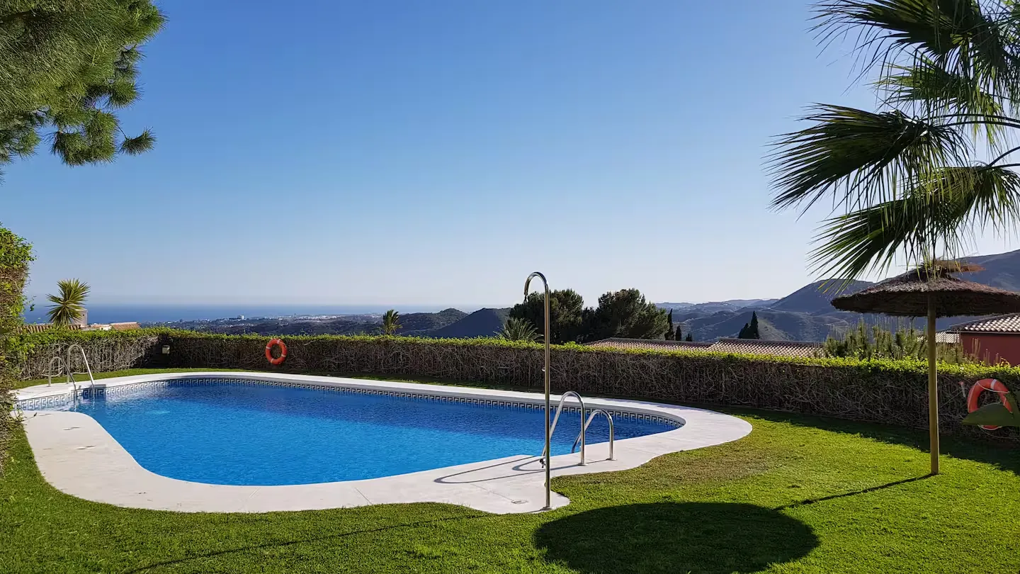 Piscina comunitaria con césped, palmeras y el mar al fondo