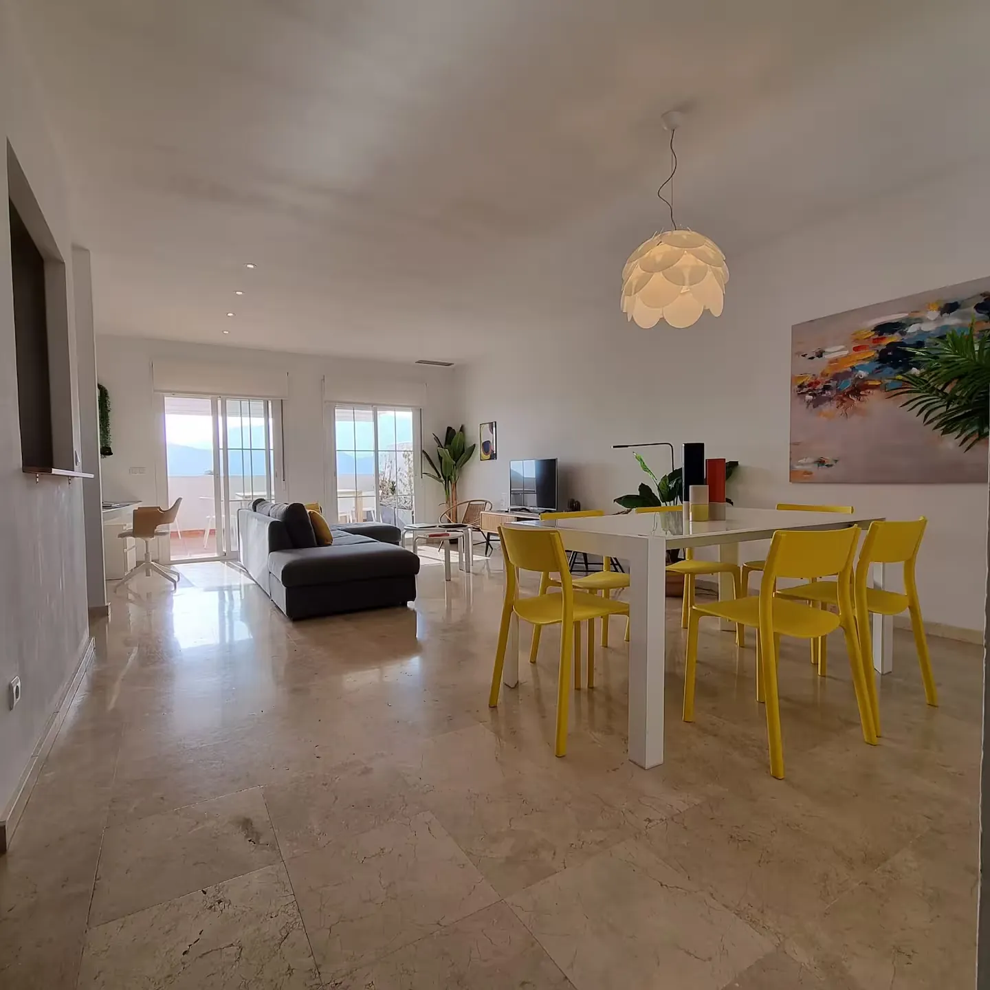 Salón comedor amplio con mesa blanca, sillas amarillas y balcón con vistas